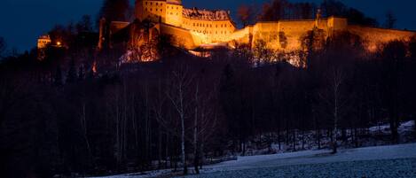A historic castle with a fortified wall, a large central building, and a smaller structure to the left.