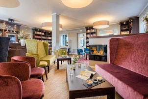 A modern lounge area with a fireplace, plush seating, a coffee table with snacks, and a bookshelf.