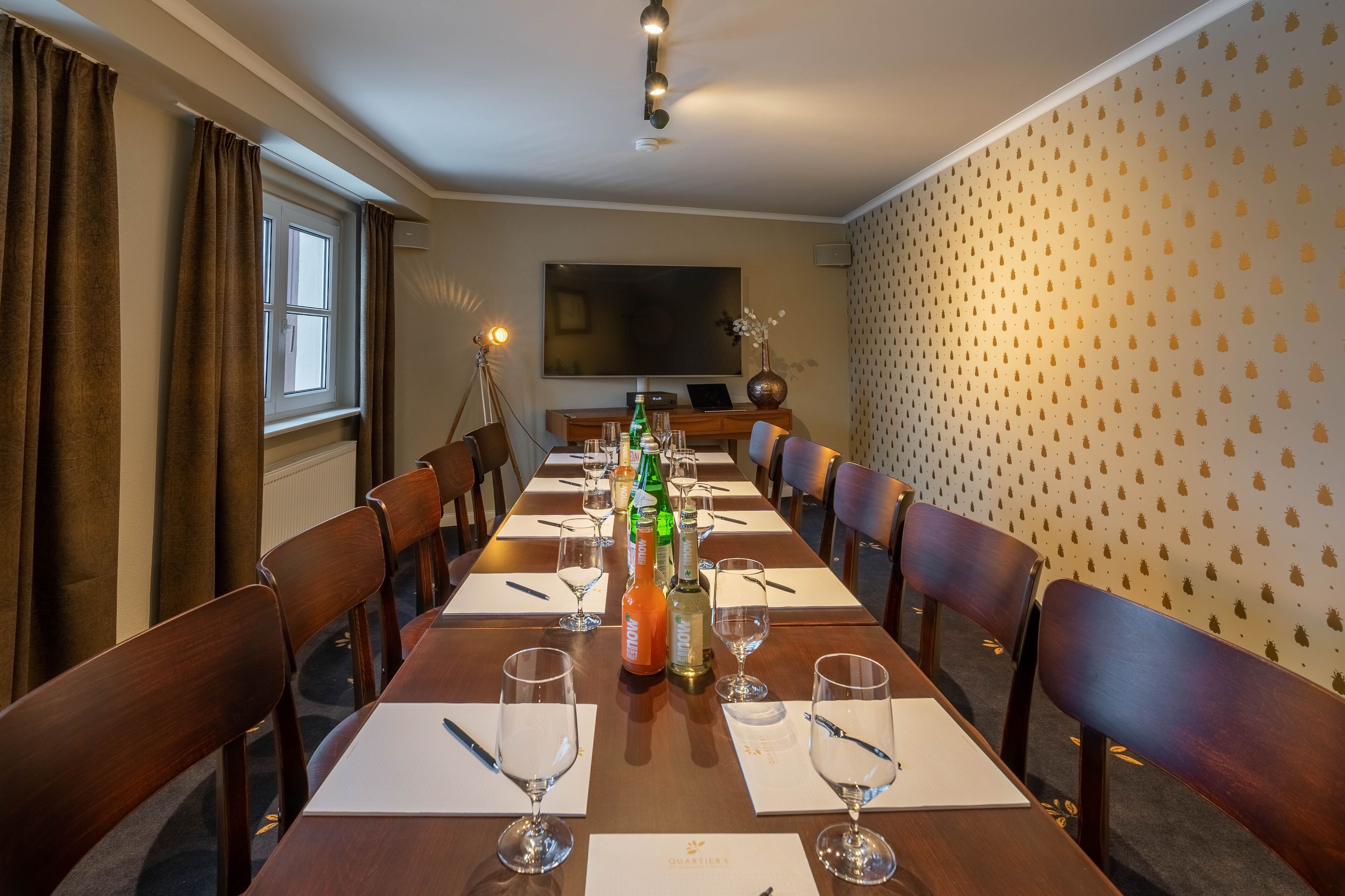 Een vergaderruimte met een lange tafel, stoelen, een scherm voor een projecter en een muur met een ananaspatroon.