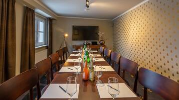 Een vergaderruimte met een lange tafel, stoelen, een scherm voor een projecter en een muur met een ananaspatroon.