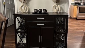 Un mueble negro de madera con puertas de cristal, dos jarrones decorativos con plumas de pampa y un espejo encima.