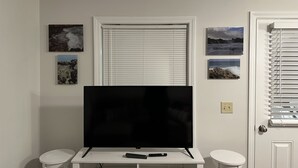 Una habitación con un televisor de pantalla plana sobre un soporte blanco, una puerta con ventana y tres cuadros en la pared.