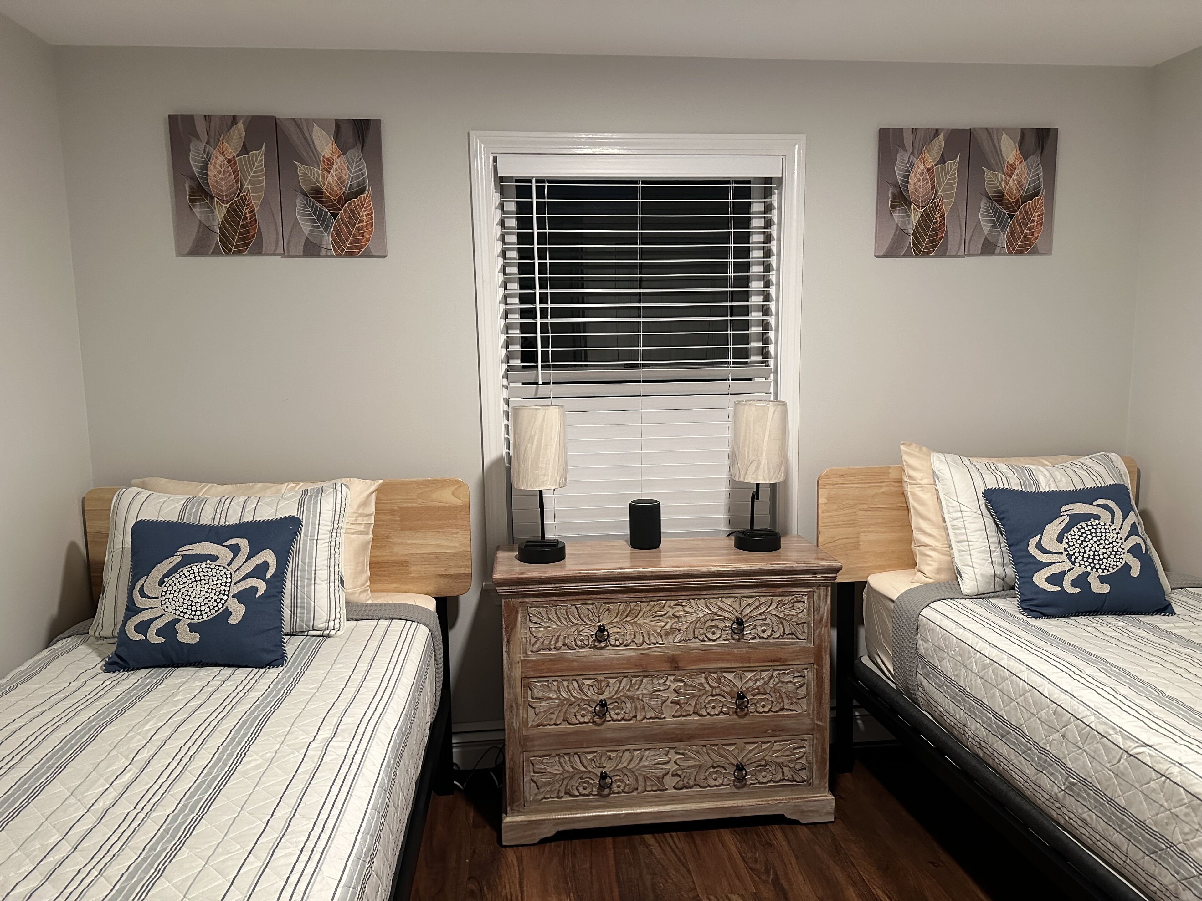 A bedroom with two beds, a nightstand, a dresser, and a window with blinds.