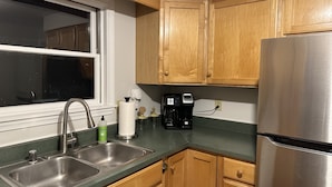Una cocina con armarios de madera, un lavamanos de acero inoxidable, una cafetera y un refrigerador.