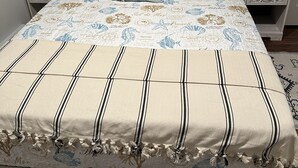 Una cama con edredón floral y a rayas, dos mesitas de noche con lámparas y un adorno en la pared.