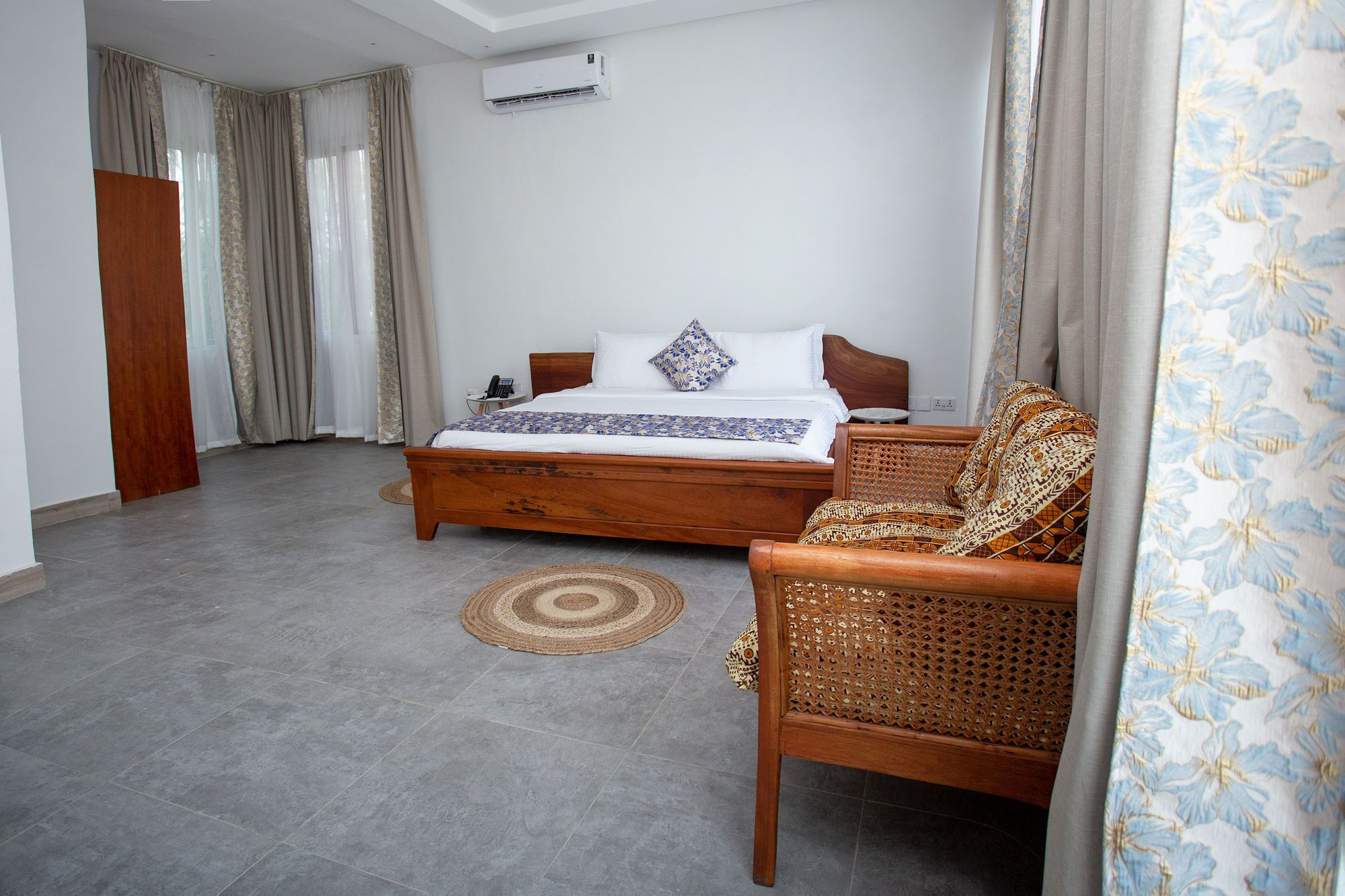 A bedroom with a wooden bed, a wicker chair, a patterned rug, and a window with curtains.