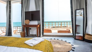 A hotel room with a bed, a TV, a table, and a view of the ocean. - La Villa Aphro Ghana (Kokrobite)