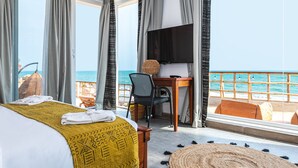 A hotel room with a bed, a desk, a TV, and a view of the sea. - La Villa Aphro Ghana (Kokrobite)