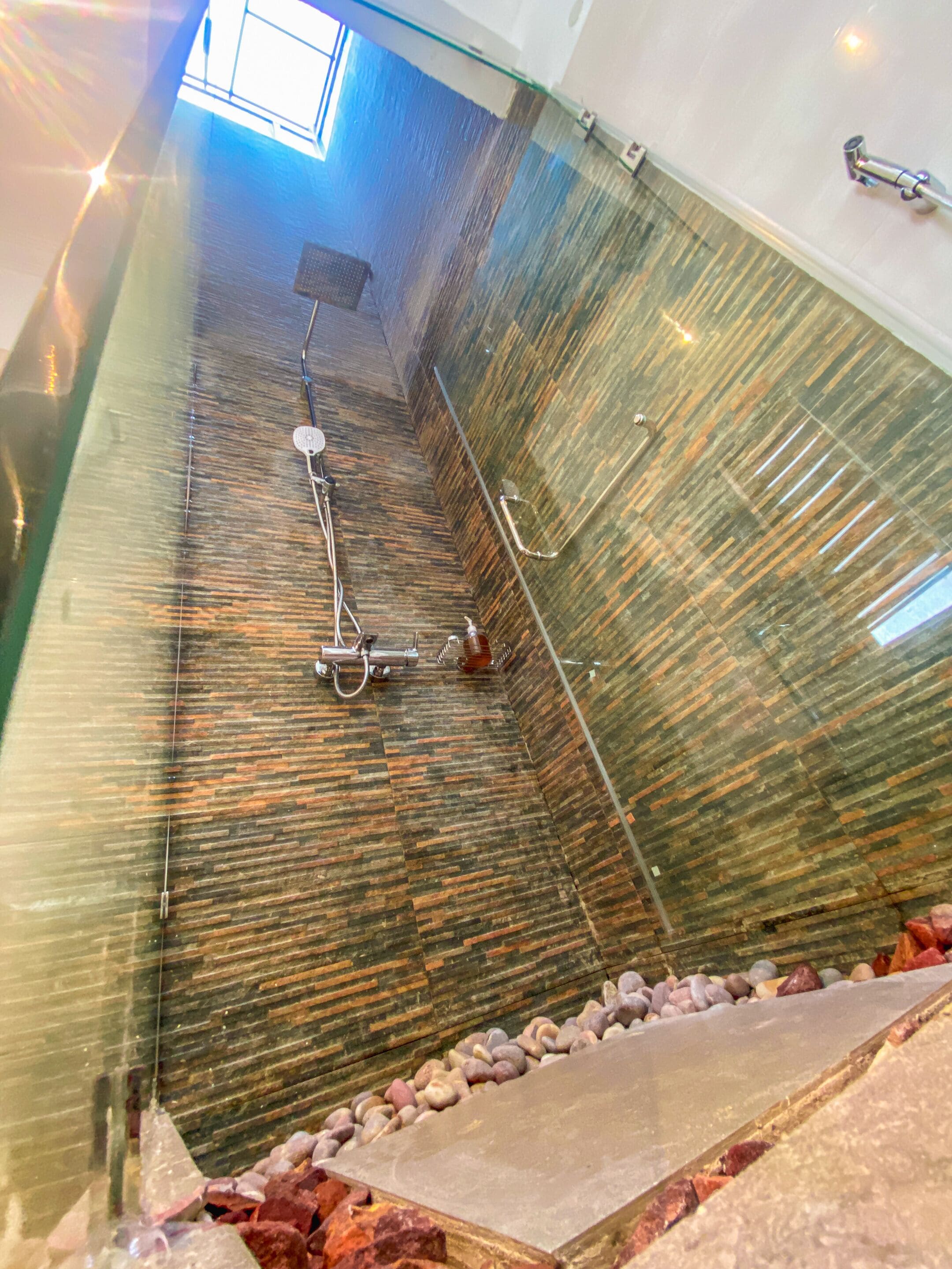 A modern bathroom with a glass-enclosed shower, a built-in sink, and a stone-tiled floor.