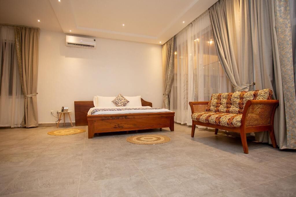 A bedroom with a bed, a chair, a small table, and a window with curtains.