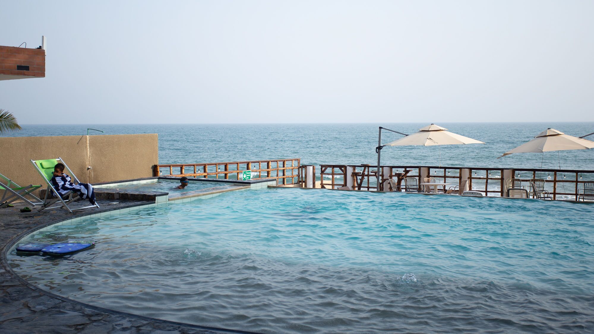 Ein Schwimmbad mit Holzterrasse und Liegestühlen mit Blick aufs Meer.