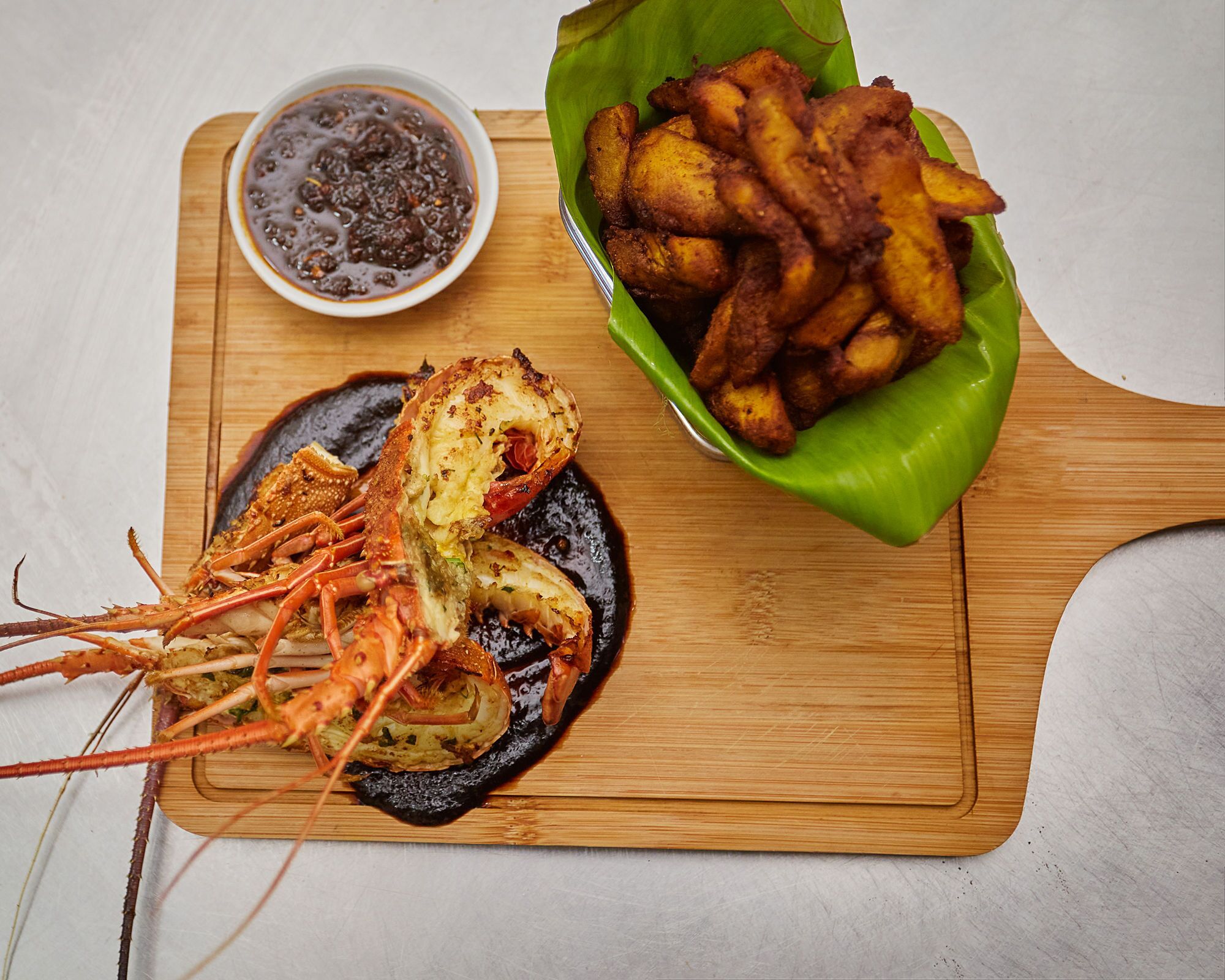 A lobster on a wooden board with a side of fries and a bowl of sauce.