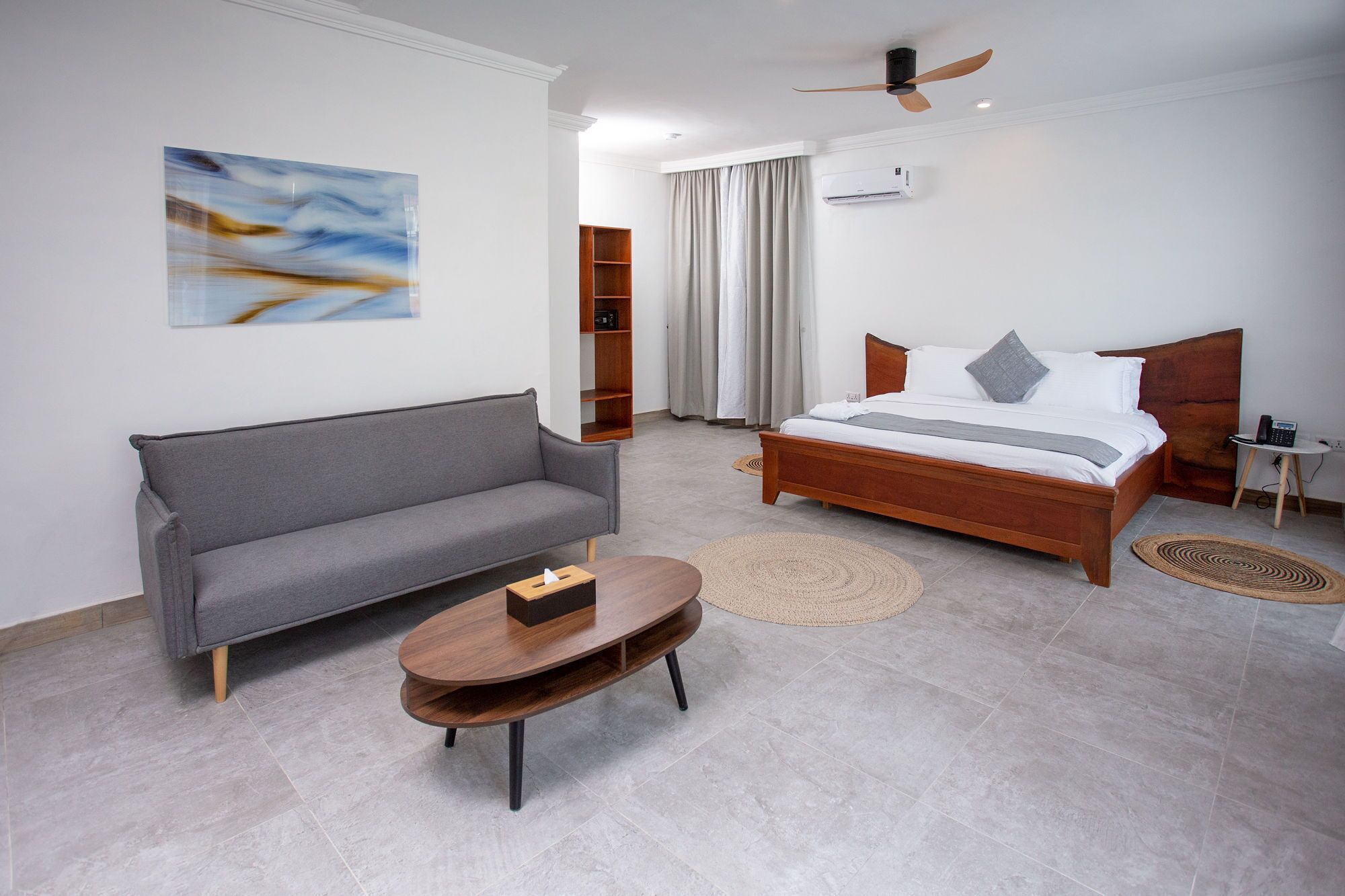 Un dormitorio moderno con un sofá gris, una cama de madera, una mesa de centro redonda y un ventilador de techo.