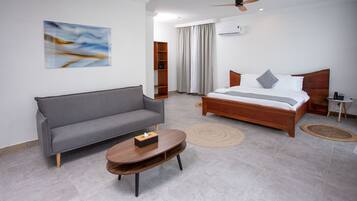 Un dormitorio moderno con un sofá gris, una cama de madera, una mesa de centro redonda y un ventilador de techo.