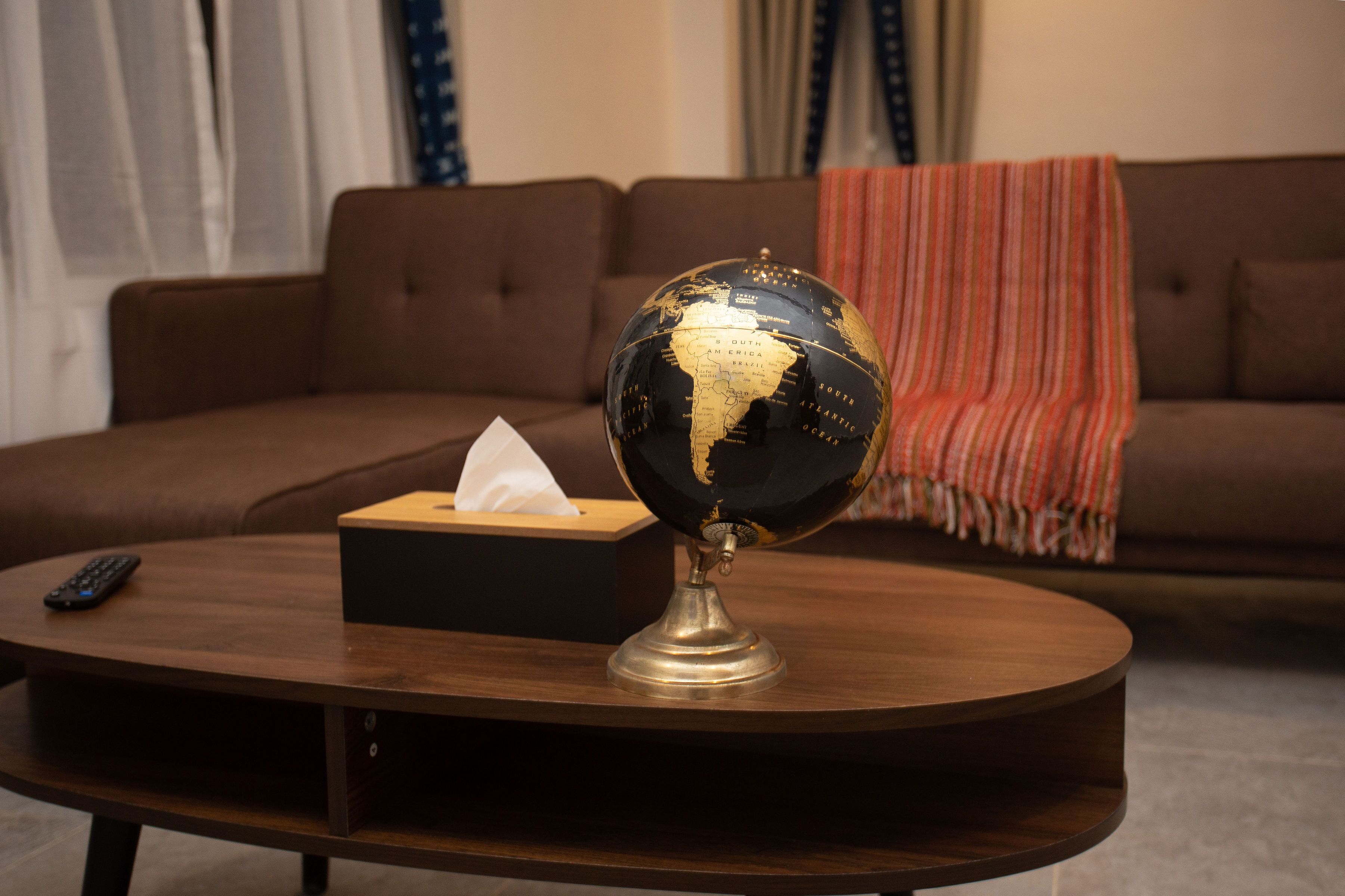 A globe on a wooden coffee table with a tissue box and a remote control.