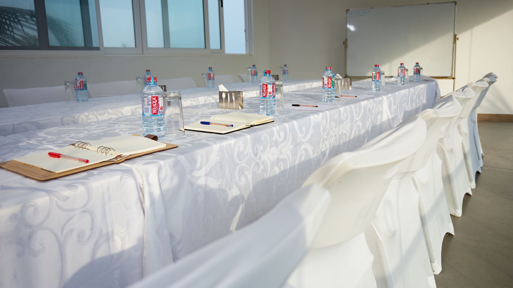 A conference room with a long table set for a meeting, equipped with water bottles, notepads, and pens.