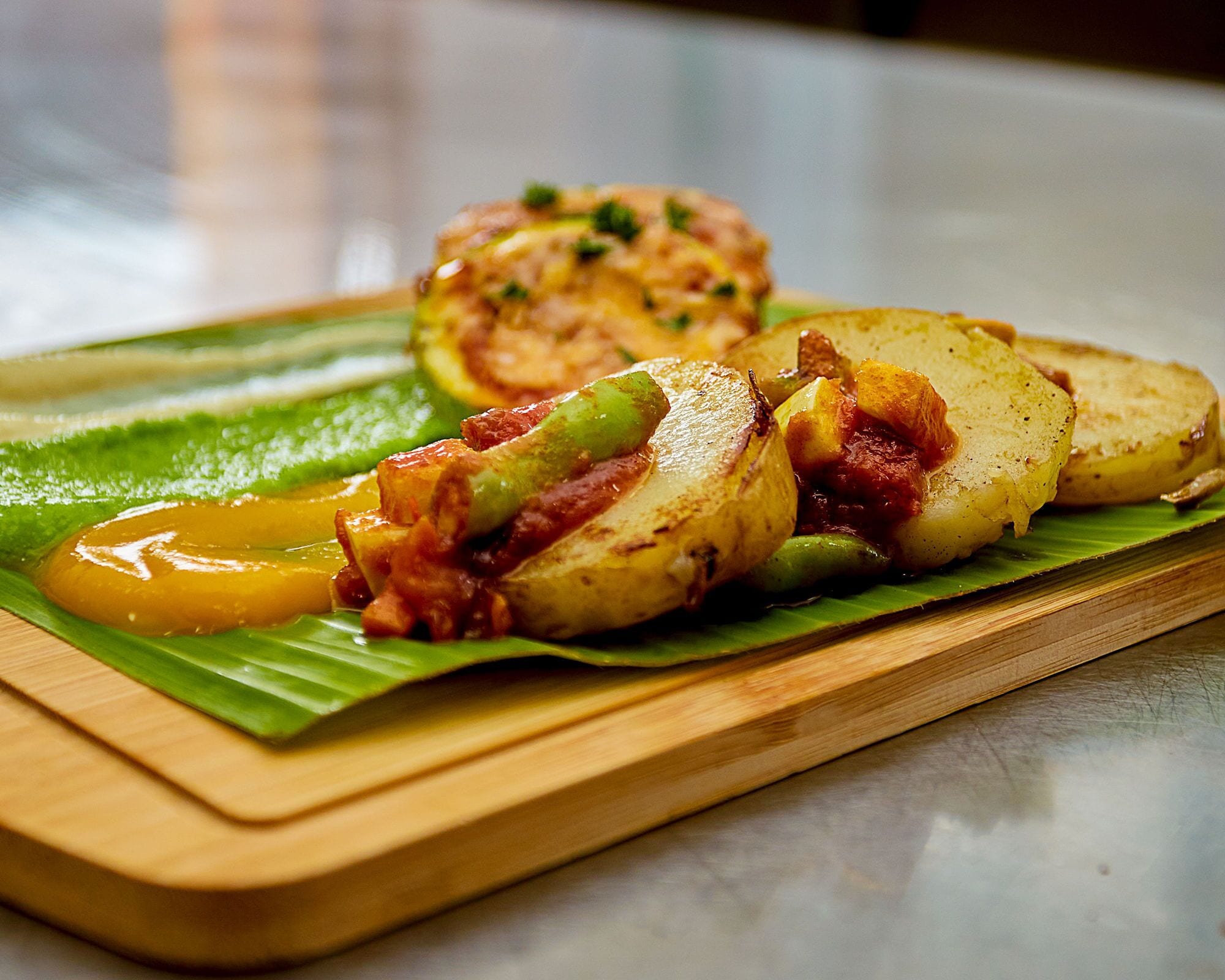 Una tabla de madera con papas en rodajas y un vegetal relleno sobre una hoja verde.