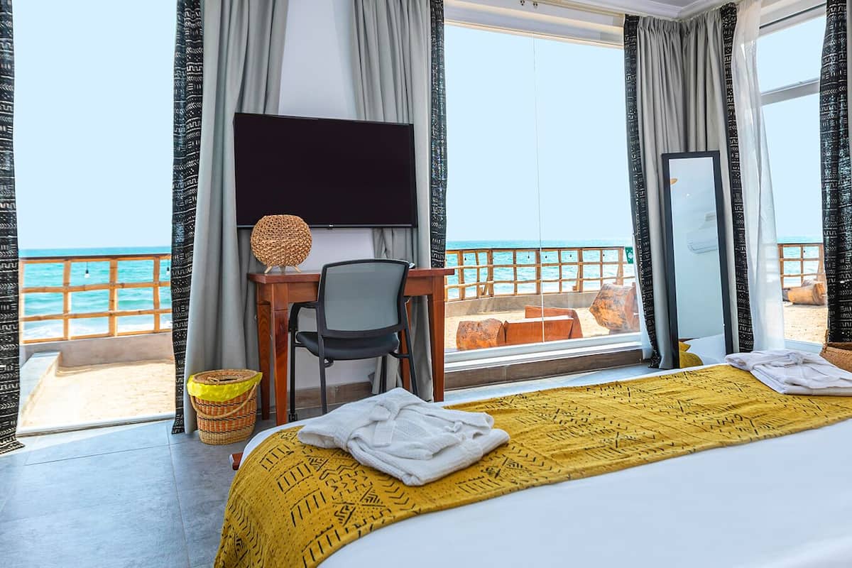 Habitación de hotel con cama, escritorio, silla, televisor y balcón con vista al mar.