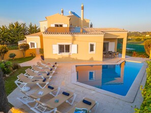 Una villa moderna con piscina, tumbonas y jardín.