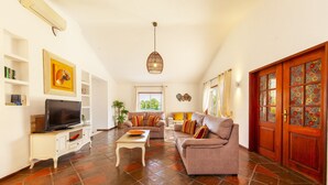 A spacious living room with a television, sofa, and coffee table. There is a wooden door with stained glass windows and a ceiling fan. - Peaceful villa with heatable pool in Galé (Albufeira)