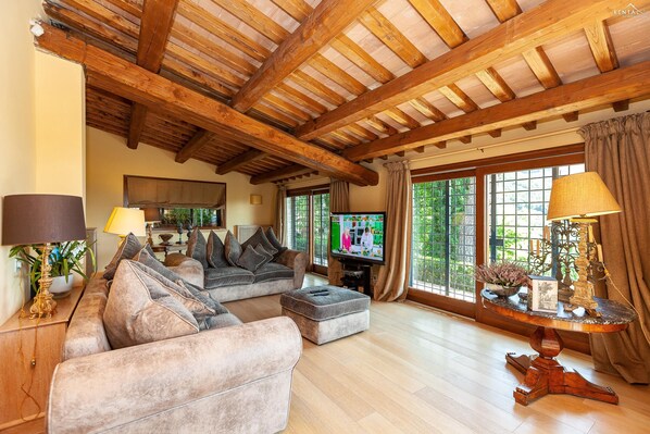 Amplia sala de estar con techo de madera, un ventanal con cortinas, un sofá, un televisor y una mesa con objetos decorativos.