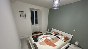 A bedroom with a bed, bedside tables, a nightstand, a window, and a hanging light fixture. - Agréable Maison à 14kms de la mer (Le Gua)