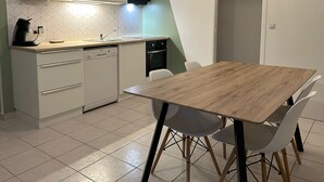 A compact kitchen with a wooden dining table, white chairs, and a dishwasher. - Agréable Maison à 14kms de la mer (Le Gua)
