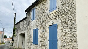 A stone building with two blue shutters and a door, a narrow street, and a utility pole. - Agréable Maison à 14kms de la mer (Le Gua)