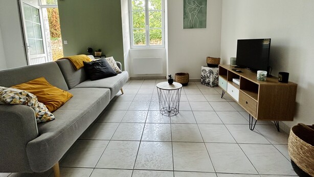 A living room with a grey sofa, a TV, and a small round table. - Agréable Maison à 14kms de la mer (Le Gua)