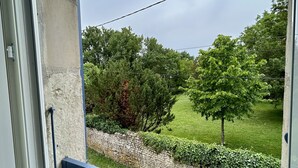 A window with a view of a stone wall, a grassy area, and trees. - Agréable Maison à 14kms de la mer (Le Gua)