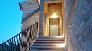 Un escalier menant à une porte surmontée d’une lumière, le tout entouré de murs en pierre.