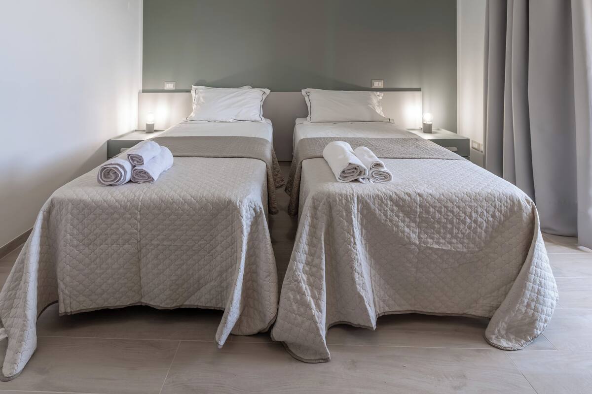 A hotel room with two beds, each with a quilted bedspread and rolled towels.