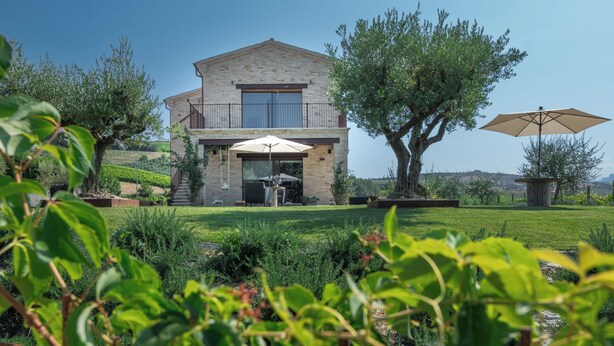 Une maison à deux étages dotée d’un balcon, d’une terrasse avec un parasol et d’un jardin bien entretenu.