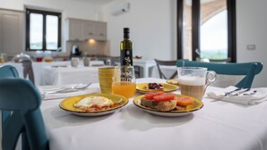 Une table dressée pour le petit-déjeuner, avec des assiettes remplies de nourriture, une bouteille et un verre de jus d’orange.