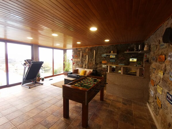 A room with a foosball table, exercise equipment, a sofa, and a stone wall with license plates.