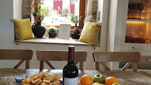A dining table with a bottle of wine, bread, fruit, and a cabinet with glasses. - CASA DO PENEDO CASTLE HOUSE (Linhares da Beira)