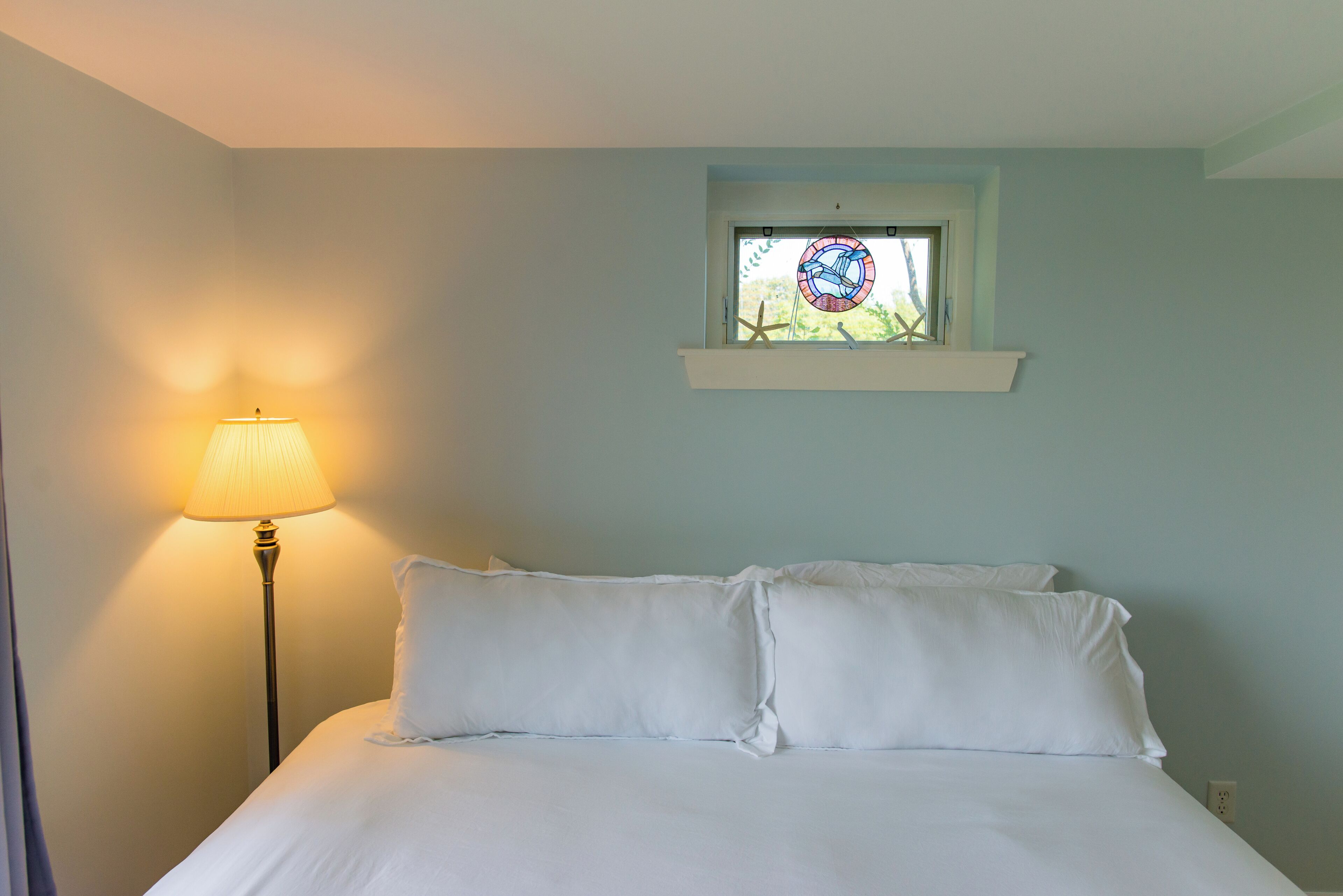 Una camera da letto con un letto, un comodino, una lampada e una finestra vista verde.