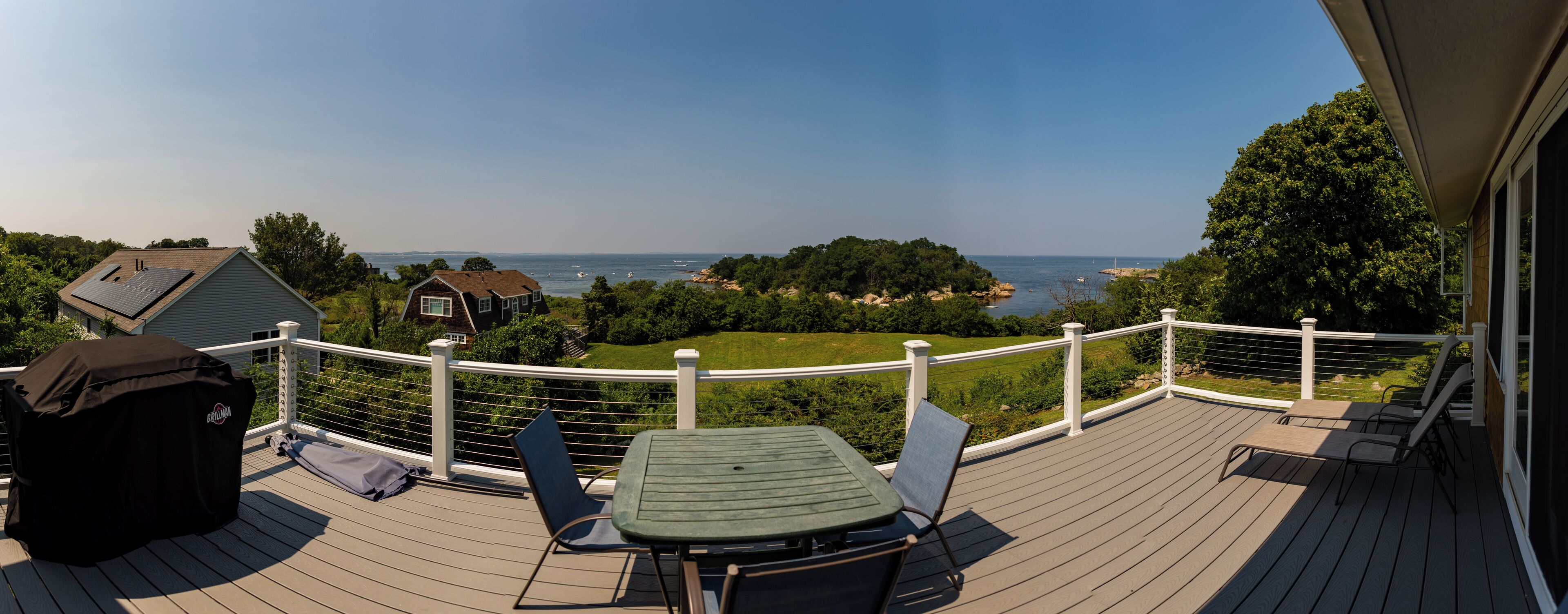 Een terras met een tafel en stoelen, met uitzicht op de kust, huizen en begroeiing.