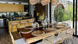 Une cuisine moderne dotée d'un îlot central, de meubles jaunes et d'un coin repas avec des chaises en osier et une table en bois pouvant accueillir six personnes.