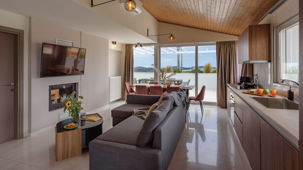 Ein modernes Wohnzimmer mit einer Couch, einem Essbereich mit Tisch und Stühlen, einer Küche mit Spüle und Arbeitsfläche sowie einem an der Wand montierten Fernseher.