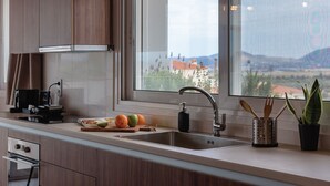 Eine moderne Küche mit Holzausstattung, einer Edelstahlspüle und einem Fenster mit Blick auf Gebäude und Berge.
