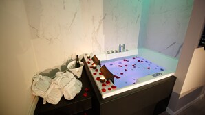 A spa area with a bathtub filled with rose petals, a bottle of champagne, and bathrobes on a counter. - Mazzini Palace (Misterbianco)