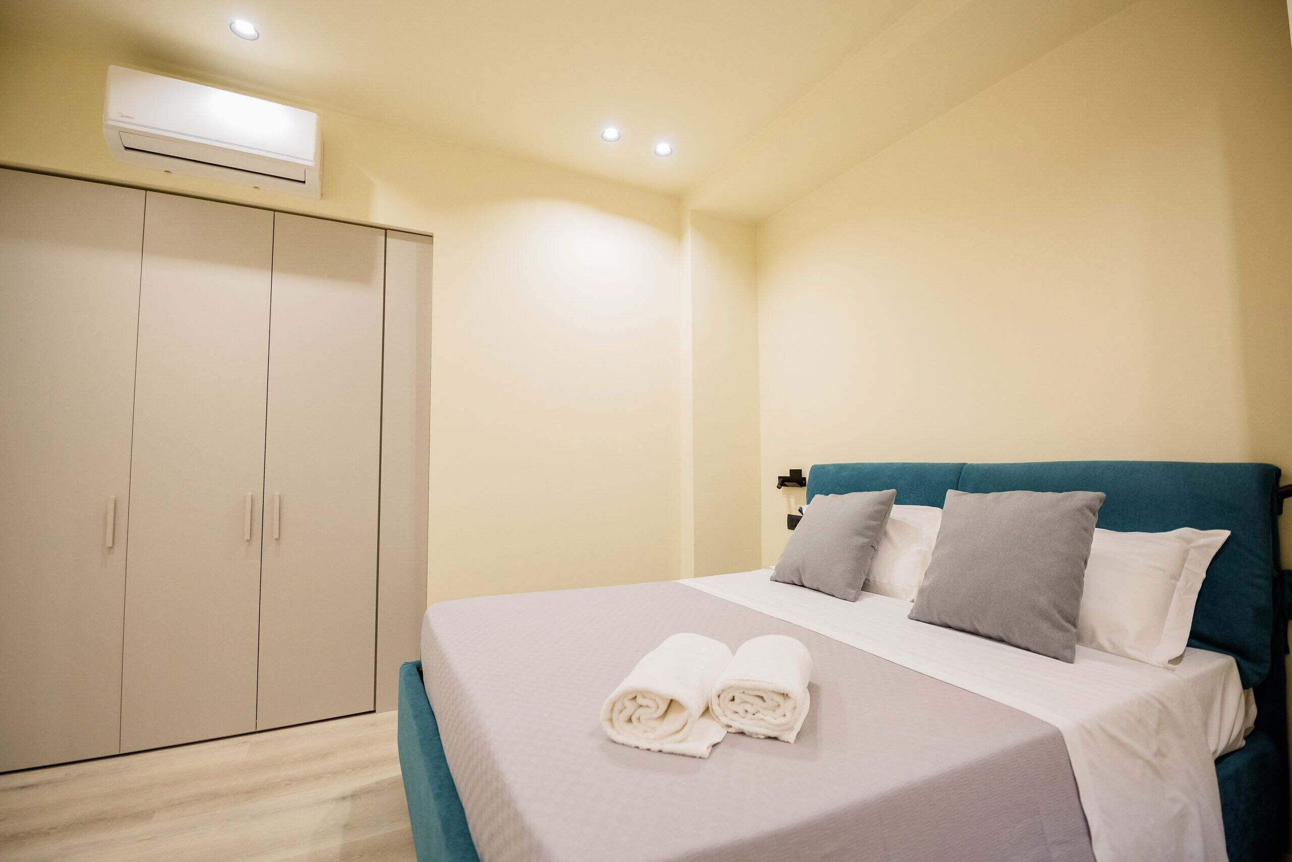 Un dormitorio con cama, almohadas, un armario y un equipo de aire acondicionado.
