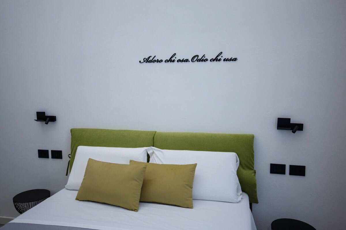 A bed with a green headboard, white and mustard pillows, and black wall-mounted lights.