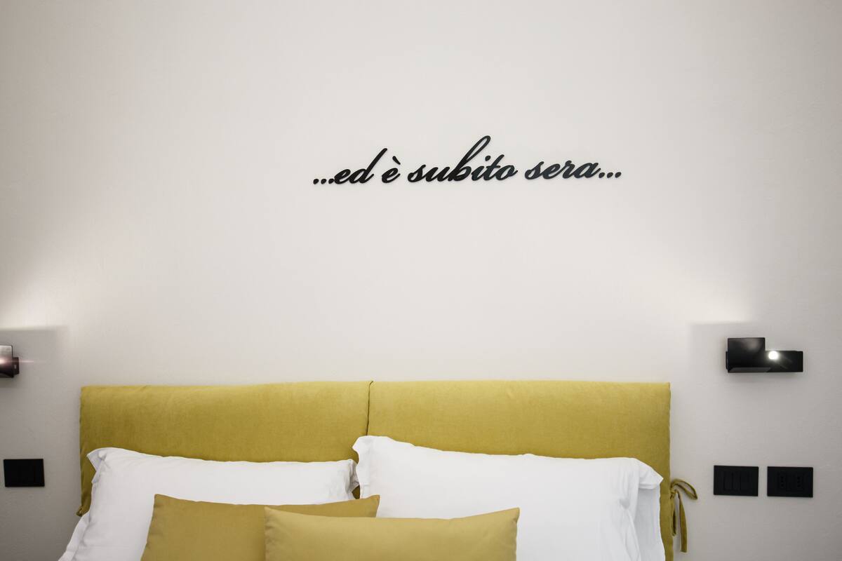 A bed with a yellow headboard, white pillows, and a wall-mounted light fixture.