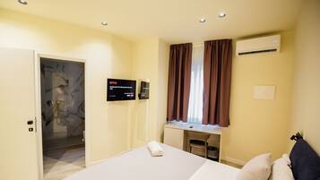 Habitación de hotel con cama, escritorio, unidad de aire acondicionado, televisor mostrando la interfaz de Netflix y zona de ducha.