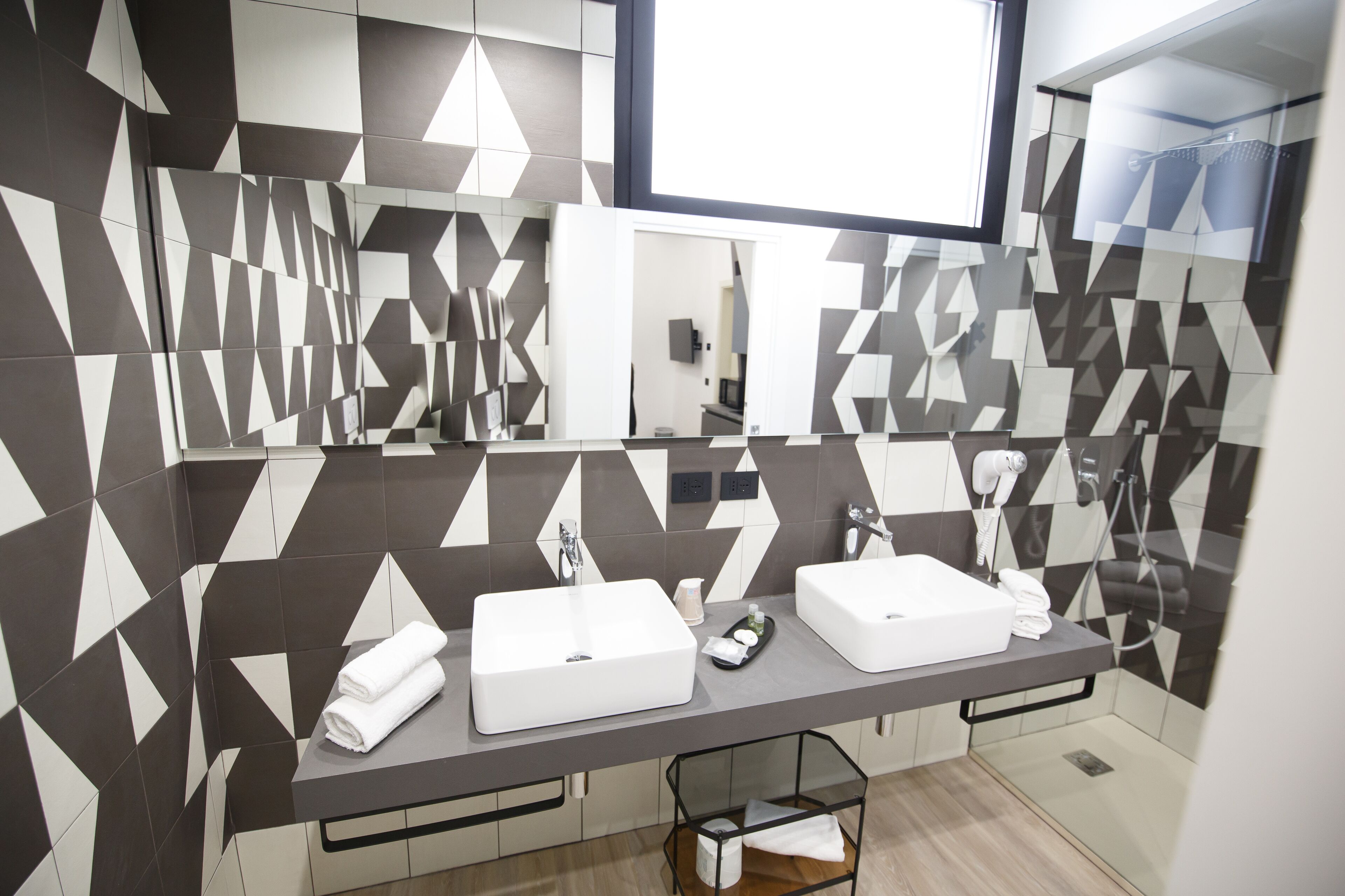 A modern bathroom with two sinks, a mirror, and geometric patterned tiles.