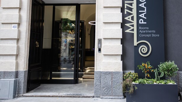 The entrance to Mazzini Palace, featuring a grand archway, a black door, and a signboard with the name and services offered. - Mazzini Palace (Misterbianco)