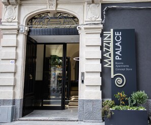 The entrance to Mazzini Palace, featuring a grand archway, a black door, and a signboard with the name and services offered. - Mazzini Palace (Misterbianco)