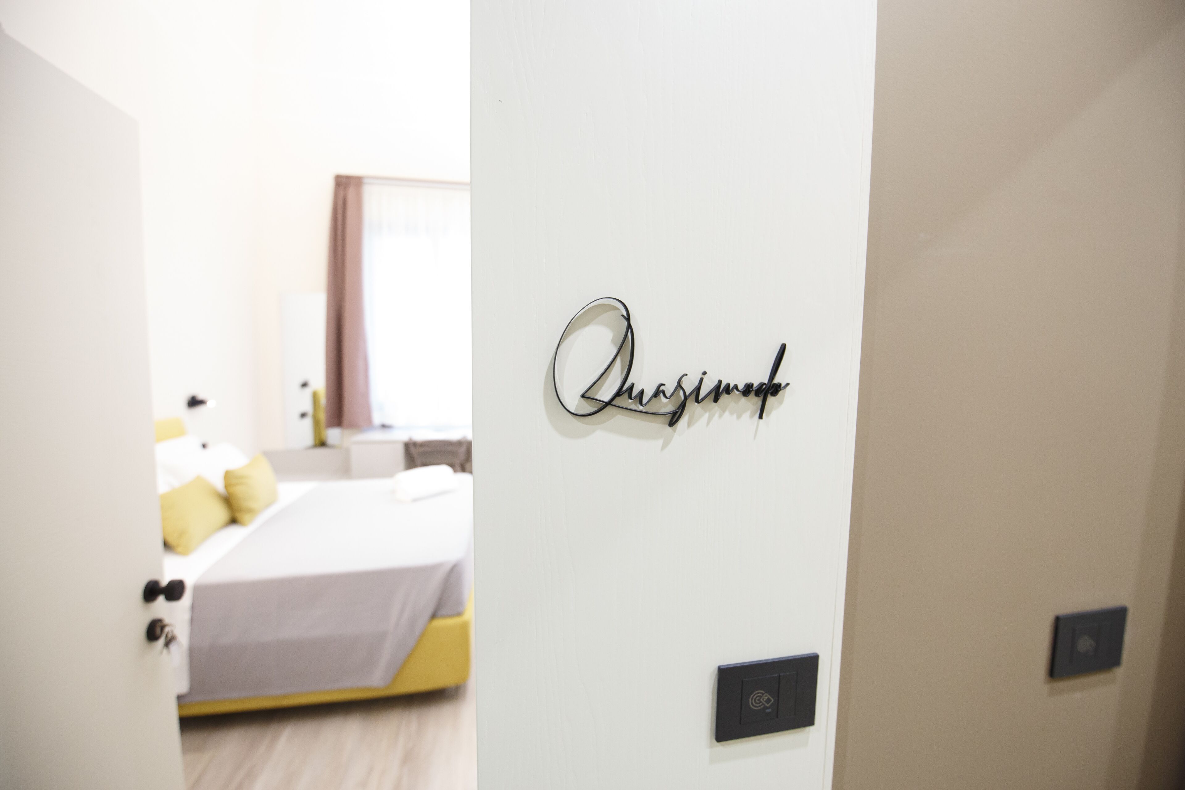 A hotel room with a bed, a bedside table, and a wall-mounted sign.